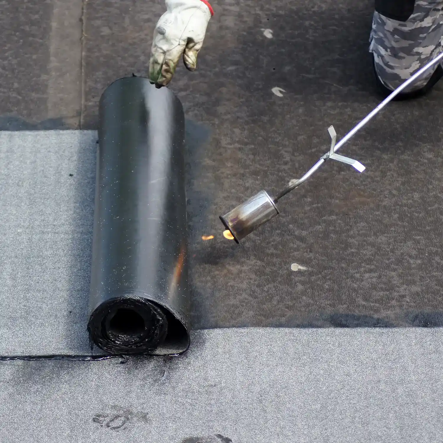 Dachdecker verschweißt Bitumenbahnen mit einem Gasbrenner auf einem Flachdach
